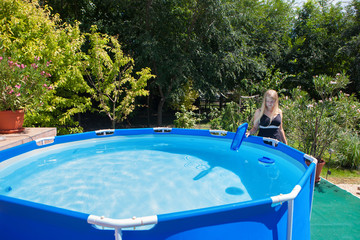 Beautiful young woman  wearing one-piece swimsuit cleaning a folding swimming pool with a skimmer