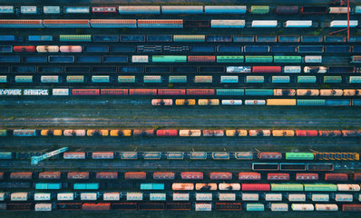 Obraz premium Zbliżenie pociągów towarowych. Widok z lotu ptaka kolorowe pociągi towarowe na stacji kolejowej. Wagony z towarami na kolei. Przemysł ciężki. Przemysłowa konceptualna scena z pociągami. Widok z góry z latającego drona