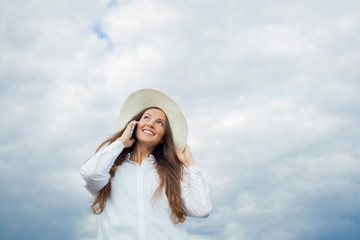 Beautiful smiling girl in a white hat with a wide brim talking on the phone on background of storm clouds