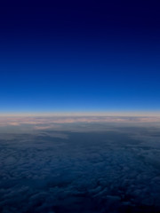 Fototapeta premium Flying high. Abstract art, fluffy clouds swirl below a vivid blue evening skyline high above earth.