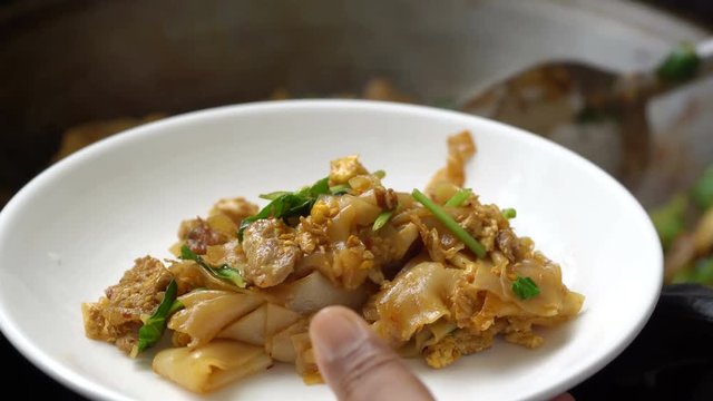 Ladling fried noodle with pork into plate, Thai food
