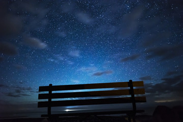Wooden park bench silhouetted in front of view of night sky full of stars