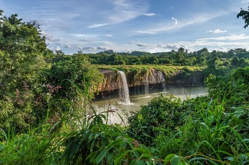 Dry Nur waterfall in Vietnam, the coast is covered with lush green tropical vegetation, against the backdrop of clouds and blue sky