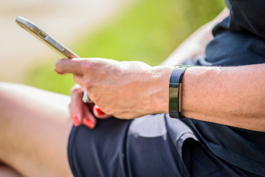 woman monitoring steps on smartwatch while holding smartphone outdoors