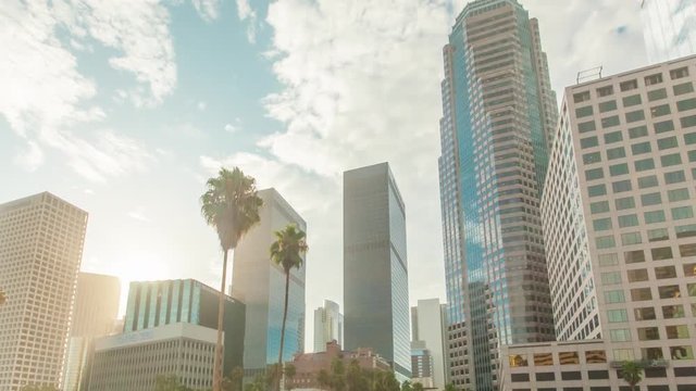 Cinematic motion timelapse or hyperlapse of downtown Los Angeles city high rise buildings at sunrise with fast moving clouds above and palm trees.