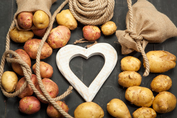 Fresh potatoes, bag and heart on a black background
