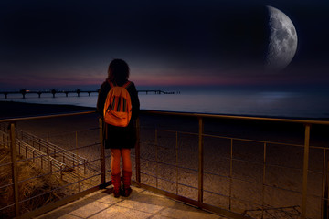 A woman stands in the night at the sea and looks at the big moon