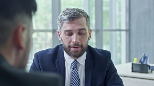PAN of bearded man in suit and tie talking to unrecognizable businesswoman and businessman asking questions during job interview 