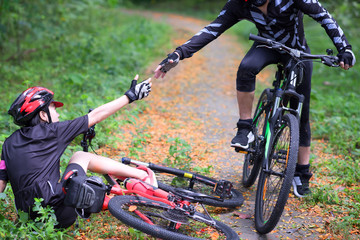 hand of cyclist woman try to reach hand of cyclist man to help supports after an accident in the jungle forest
