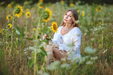 Young woman sitting in a field among sunflowers, on a bright summer day.