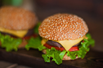 American food. Hamburger with beef patty, salad, tomato, cheese on a dark background.