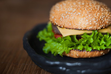 American food. Hamburger with beef patty, salad, tomato, cheese on a dark background.