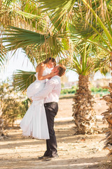 Fototapeta na wymiar Happy Bride And Groom Kissing Under Palm Trees On A Tropical Beach