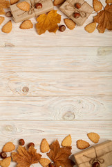 Flat lay frame of yellow leaves, cookies in the form of leaves, hazelnuts and gift boxes on a light wooden background.