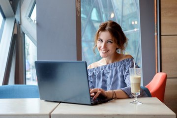 Fototapeta na wymiar Portrait of beautiful smiling woman sitting in a cafe with black laptop