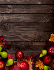 Flat lay frame of autumn crimson and yellow leaves, pears and apples on a dark wooden background.