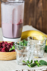 Milk cocktail of banana and raspberries in a blender. Empty glasses