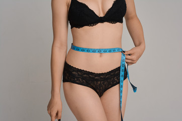 A girl with a sports figure measures her waist centimeter. Beautiful underwear. Sports girl with a...