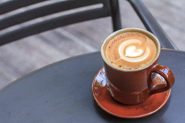 Hot latte coffee cup on black metal table in coffee shop.