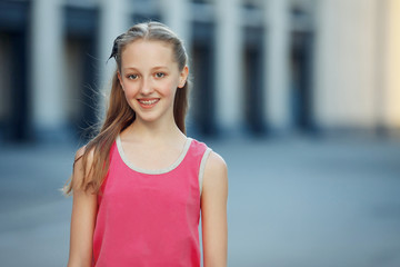 Young beautiful woman visiting a city center during a sunny day, smiling at the camera with buildings in the background.