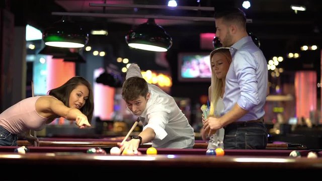 two happy young couples playing billiard together, men doing a good shot
