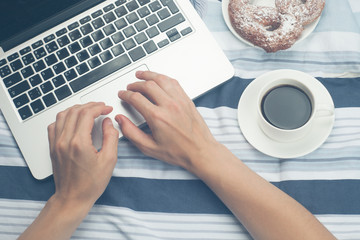 Woman using laptop on her bed, technology, holidays, blogger style and winter concept - cozy bedroom with laptop computer with female hands, coffee cup and fresh bakery