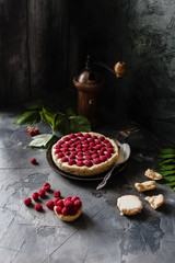raspberry tart with fresh beries on old black pan with coffee grinder, spoon. flowers and crushed tart on a grey background