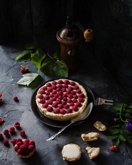 raspberry tart with fresh beries on old black pan with coffee grinder, spoon. flowers and crushed...