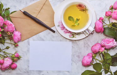 Vintage mockup. Blank paper and envelope, tea cup, pink roses, pen. Wedding invitation