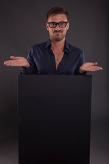 Young surprised man portrait of a confident businessman showing presentation, pointing placard black background. Ideal for banners, registration forms, presentation, landings, presenting concept.