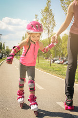 Mother and her little daughter inline skating on sidewalk. Mother and daughter enjoying in spring...