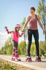 Mother and her little daughter inline skating on sidewalk. Mother and daughter enjoying in spring...