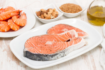 raw salmon, shrimps, nuts and olive oil on wooden background