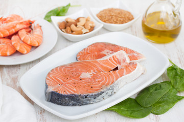 raw salmon, shrimps, nuts and olive oil on wooden background