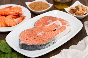 raw salmon, shrimps, nuts and olive oil on wooden background