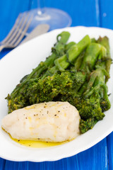 boiled fish with greens and olive oil on white dish on wooden background