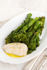 boiled fish with greens and olive oil on white dish on wooden background
