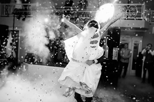 Newly married couple dancing on their wedding party with heavy smoke and multicolored lights on the background. Black and white photo.