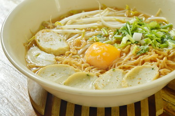 boiled instant noodles topping egg yolk and slice fish line in spicy soup