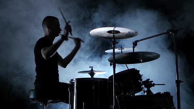 Professional musician plays music on drums . Smoky background. Side view. Silhouette. Back light. Slow motion