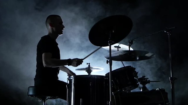 Energetic musician plays good music on drums. Black smoky background . Side view. Silhouette. Slow motion