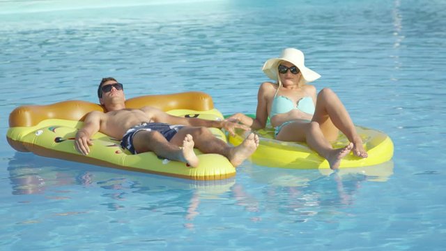 CLOSE UP: Fit young couple laying and relaxing on pizza and pineapple floaties in pool. Girlfriend and boyfriend enjoying summer vacation on fun colorful floats floating in water on hot sunny day