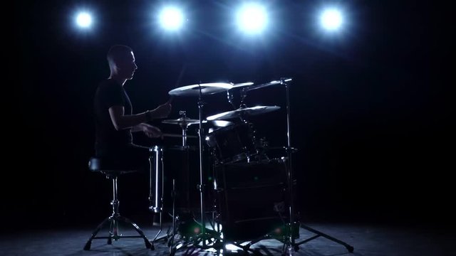 Drummer plays the melody on the drums energetically. Black background. Back light. Silhouette. Slow motion