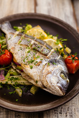 Baked whole fish, served with roasted vegetables and lemon.