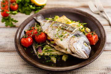 Baked whole fish, served with roasted vegetables and lemon.