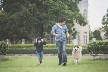father and son walking with a siberian husky don in the park