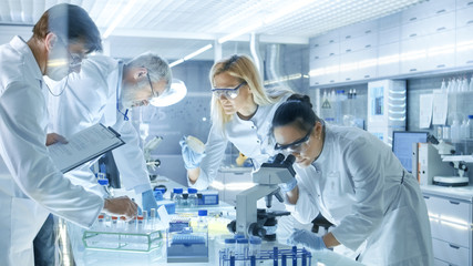Fototapeta Team of Medical Research Scientists Work on a New Generation Disease Cure. They use Microscope, Test Tubes, Micropipette and Writing Down Analysis Results. Laboratory Looks Busy, Bright and Modern. obraz
