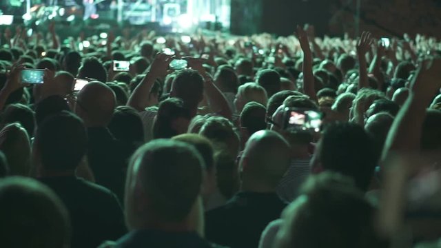 A crowd of spectators near the stage listen to the performance dance and take pictures of the performance on smartphones