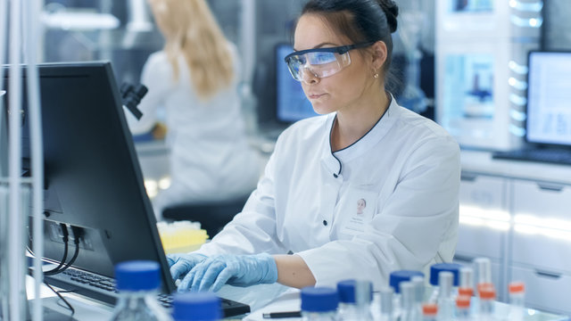 Medical Research Scientist Typing Information Obtained From New Experimental Drug Trial. She Works In A Bright And Modern Laboratory.