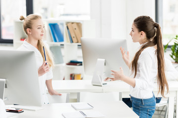 side view of teen girls discussing task together while standing in computer class